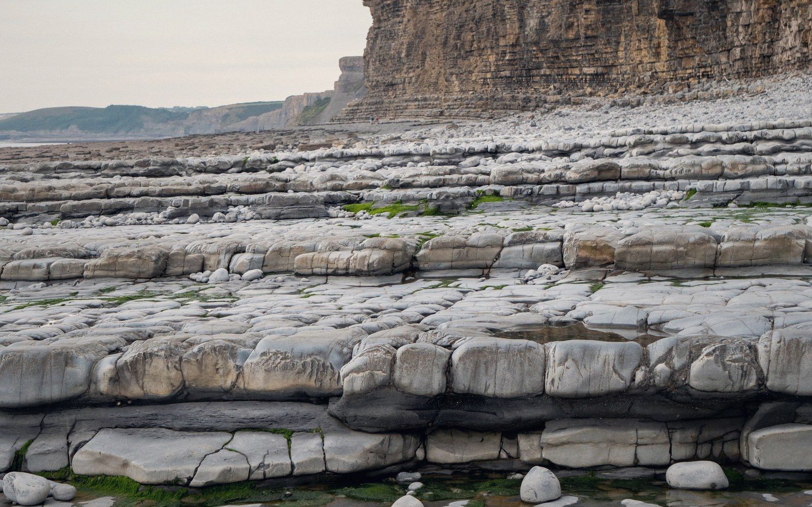 Layered limestone shelves stretch toward tall striated cliffs at the shoreline